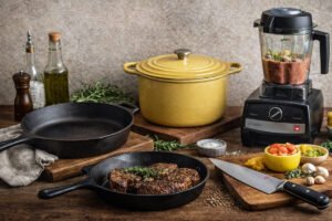 Buy it once home goods including cast iron skillet, Dutch oven, chef’s knife, and high-powered blender on a rustic kitchen counter